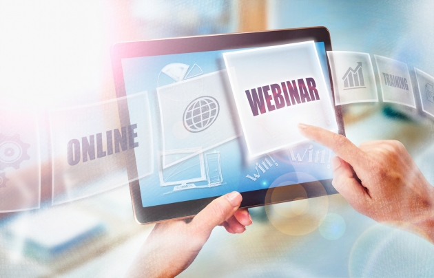 Na zdjęciu tablet trzymany w dłoni. Widoczne są także napisy webinar, online, training oraz obrazki.